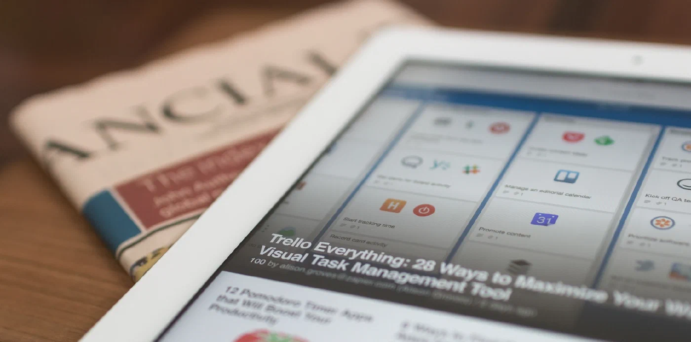 A tablet showing a productivity article beside a folded newspaper
