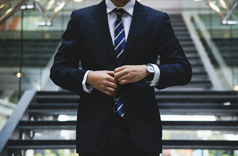 A person in a suit fastening their jacket at the foot of an office staircase