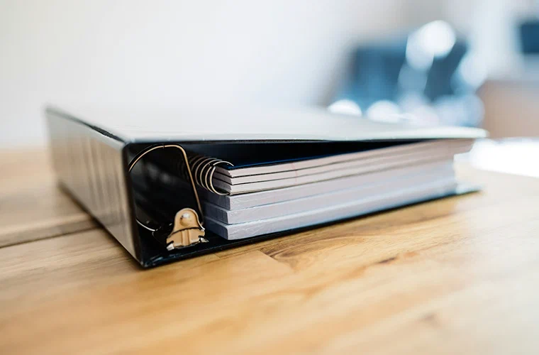 A ring binder of documents lying open on a wooden desk